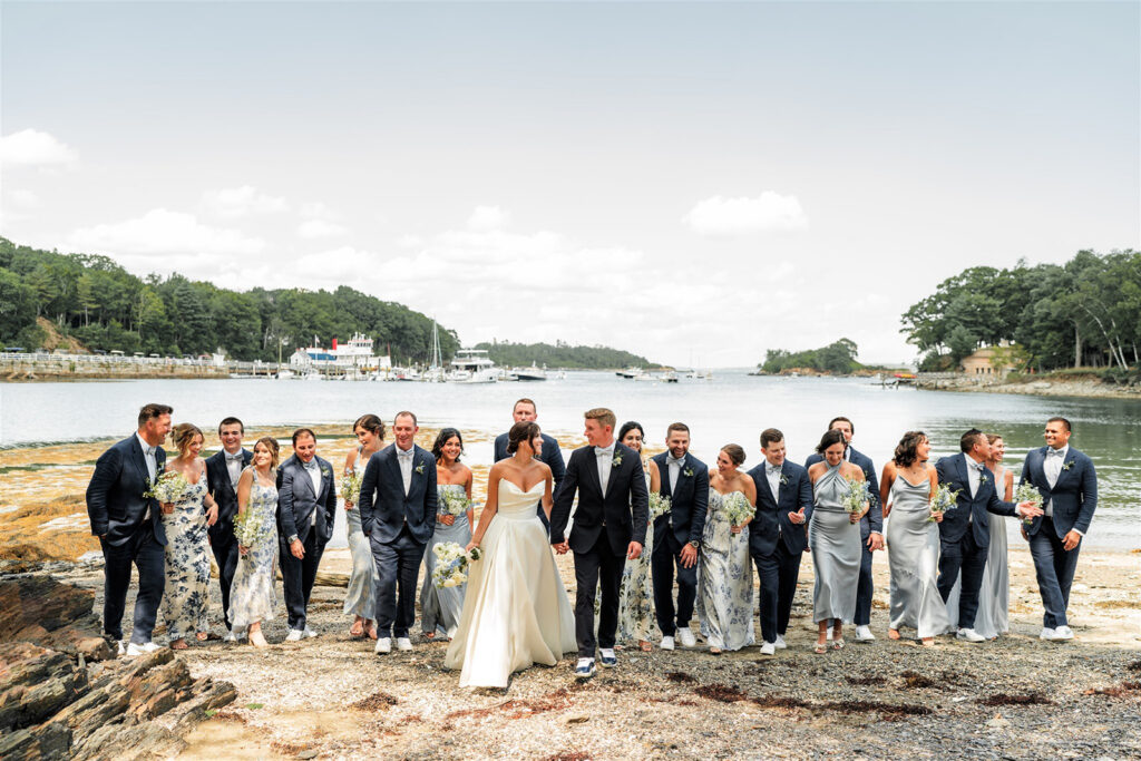 Wedding party walking together along the shoreline with boats in the background at Inn at Diamond Cove in Maine.