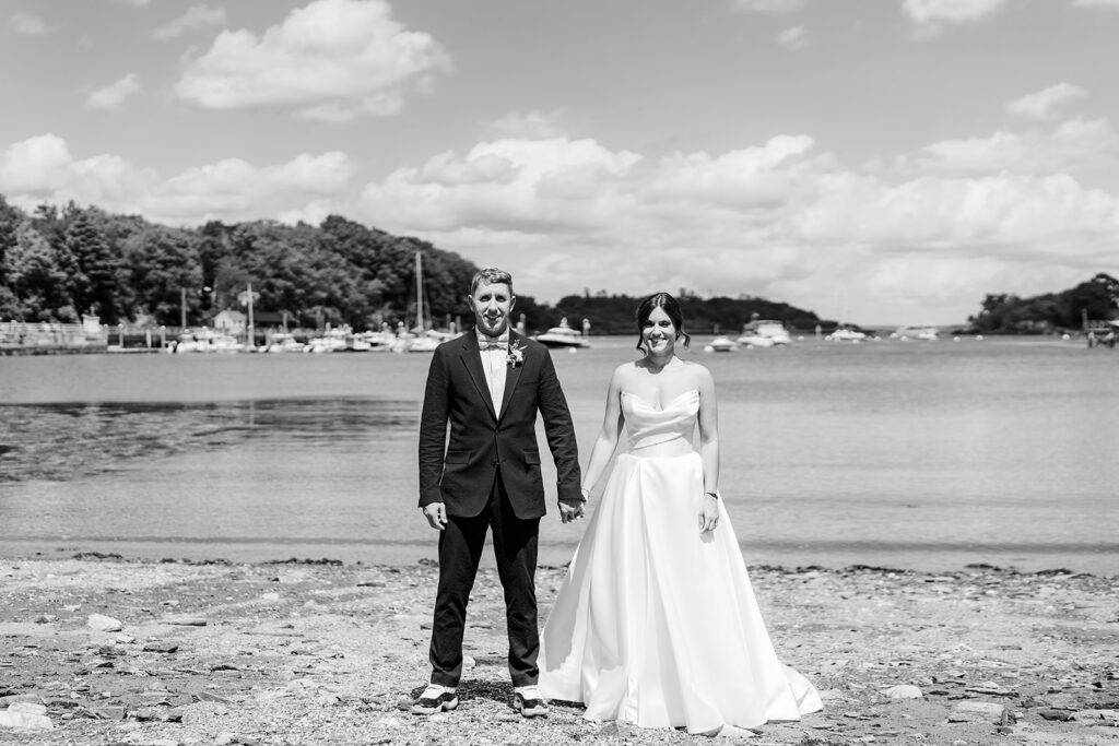 Bride and groom standing together on a rocky shoreline with harbor views at Inn at Diamond Cove in Maine.