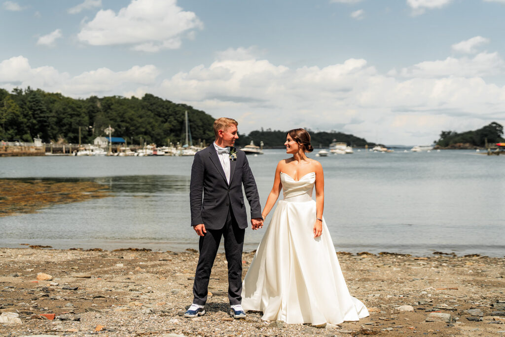 Bride and groom holding hands and smiling at each other on the beach at Inn at Diamond Cove in Maine.