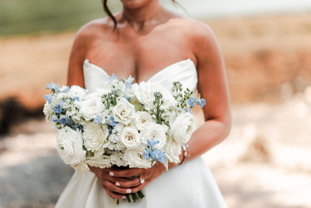 Close-up of bride holding a bouquet of white and soft blue flowers.