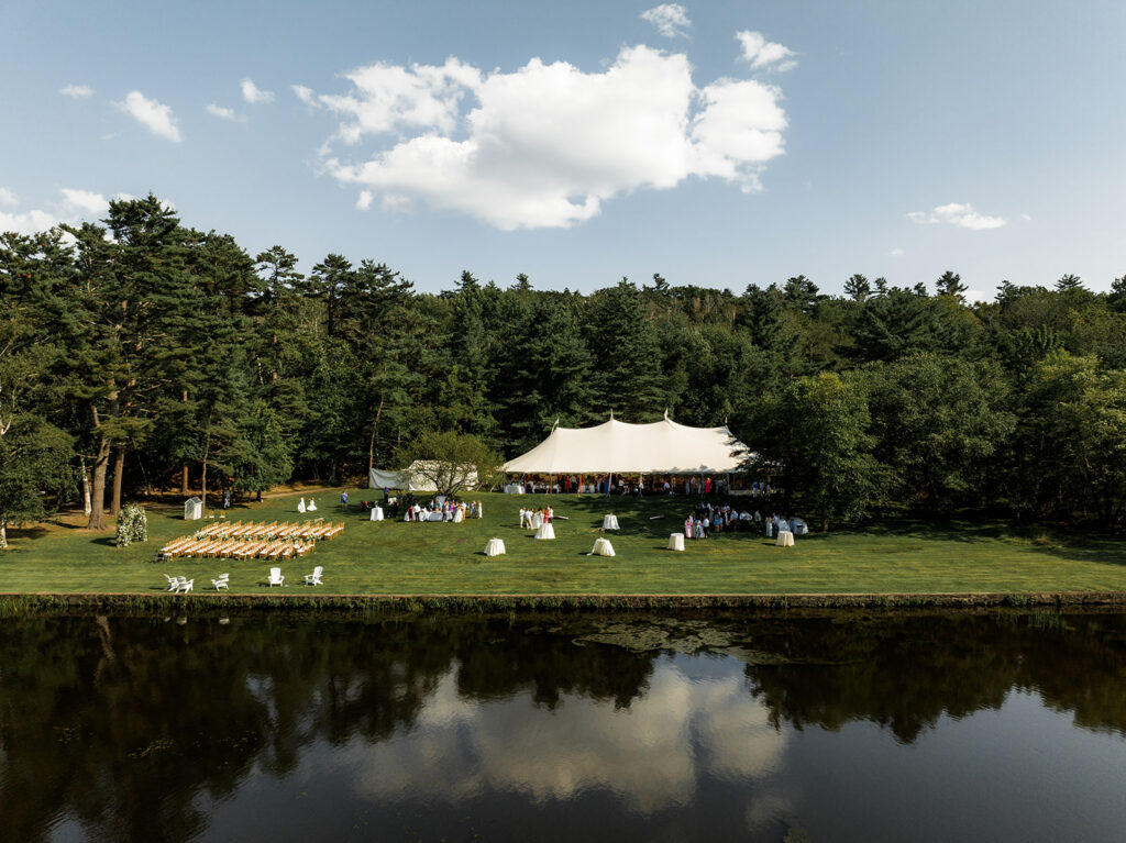 Wide view of a sailcloth tent reception set on a lawn beside a calm waterfront at Inn at Diamond Cove in Maine.