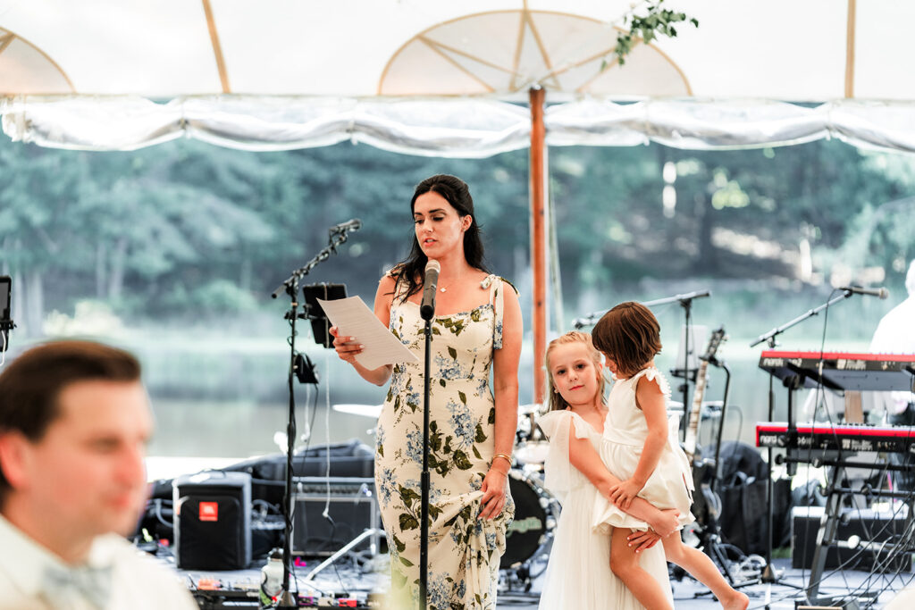Woman giving a speech while holding a child beside her inside a tent with live band equipment behind.
