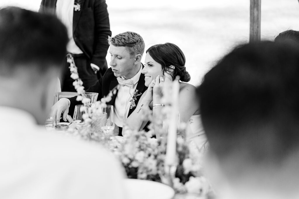 Bride and groom seated together at reception table in a candid black and white moment.