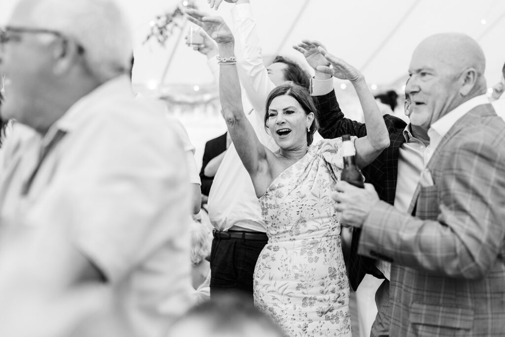 Guests dancing and cheering with raised hands during a lively reception inside a sailcloth tent.