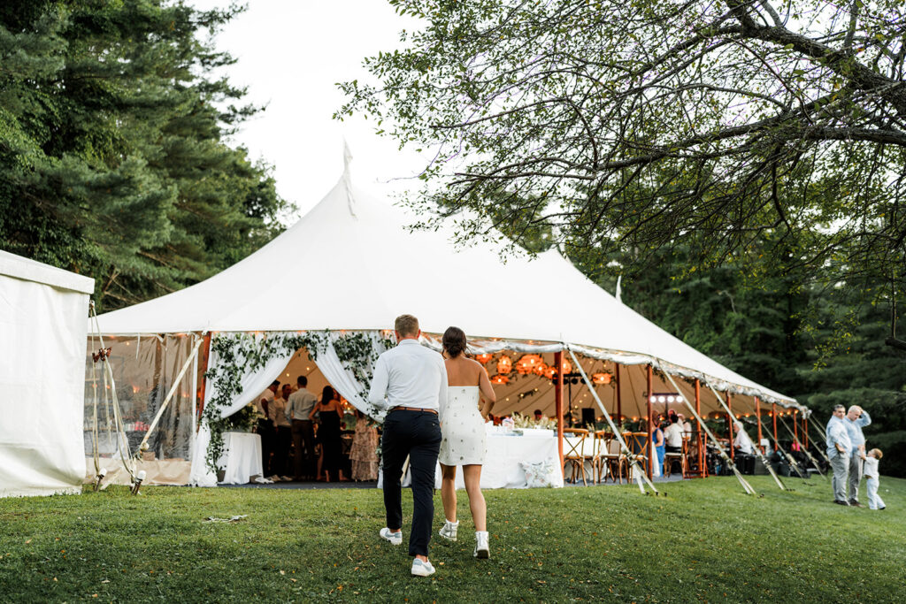 Couple walking toward a sailcloth tent glowing with string lights during the reception at Inn at Diamond Cove in Maine.