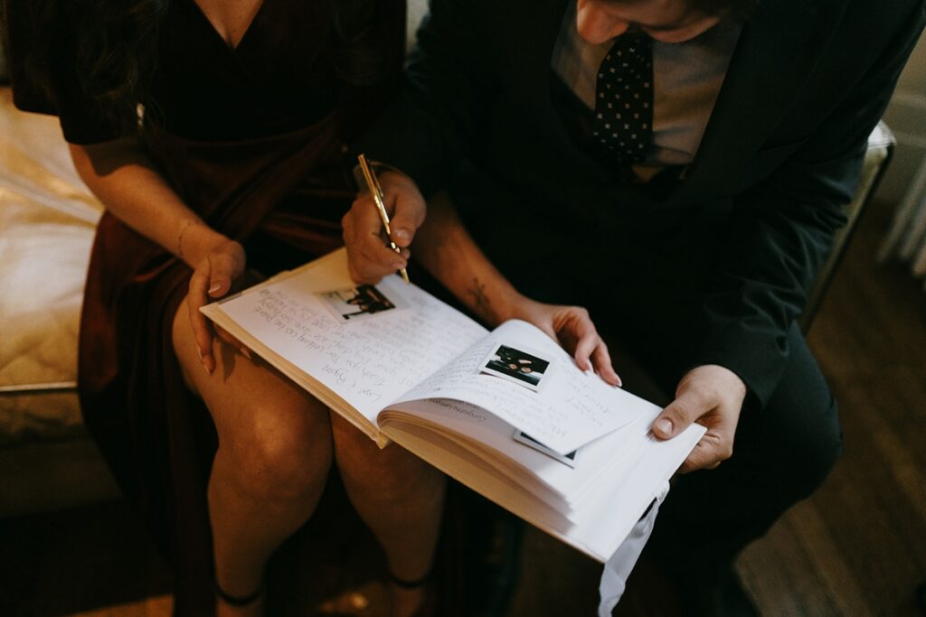 Guest writing in a wedding guestbook with instant photos attached on a couch.