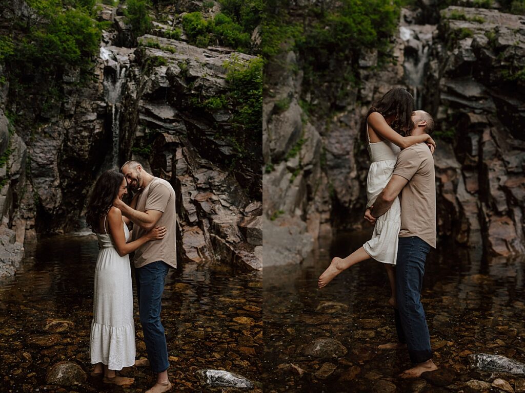 Couple standing barefoot in a rocky mountain stream beneath a waterfall and embracing as the man lifts the woman during a New Hampshire engagement session.