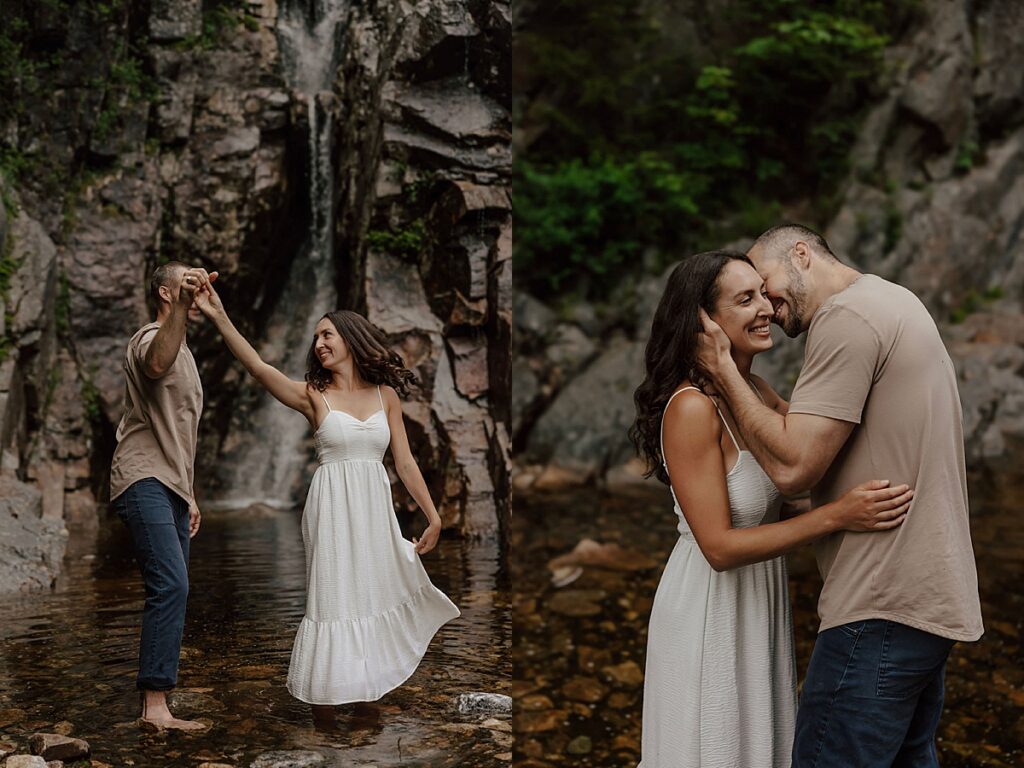 Couple dancing and holding hands in a shallow stream below a rocky waterfall and sharing a close embrace during a New Hampshire engagement session.