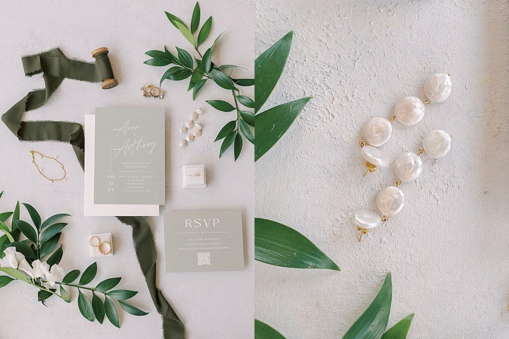 Wedding invitation suite with olive ribbon, greenery, rings, and RSVP card beside pearl drop earrings on textured surface.