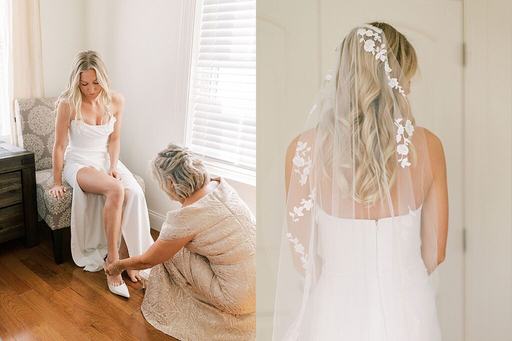 Bride seated while a woman helps with her shoes and veil detail draped over her hair and gown.