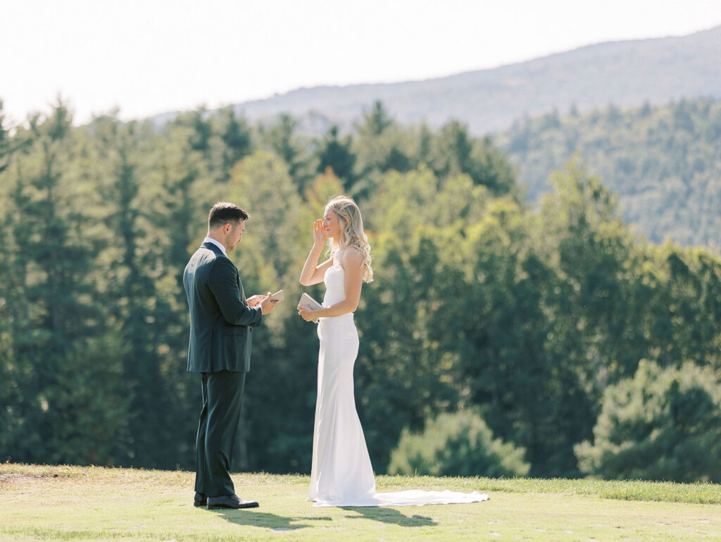 Bride wiping a tear while the groom reads vows during an intimate first look overlooking forested mountains.