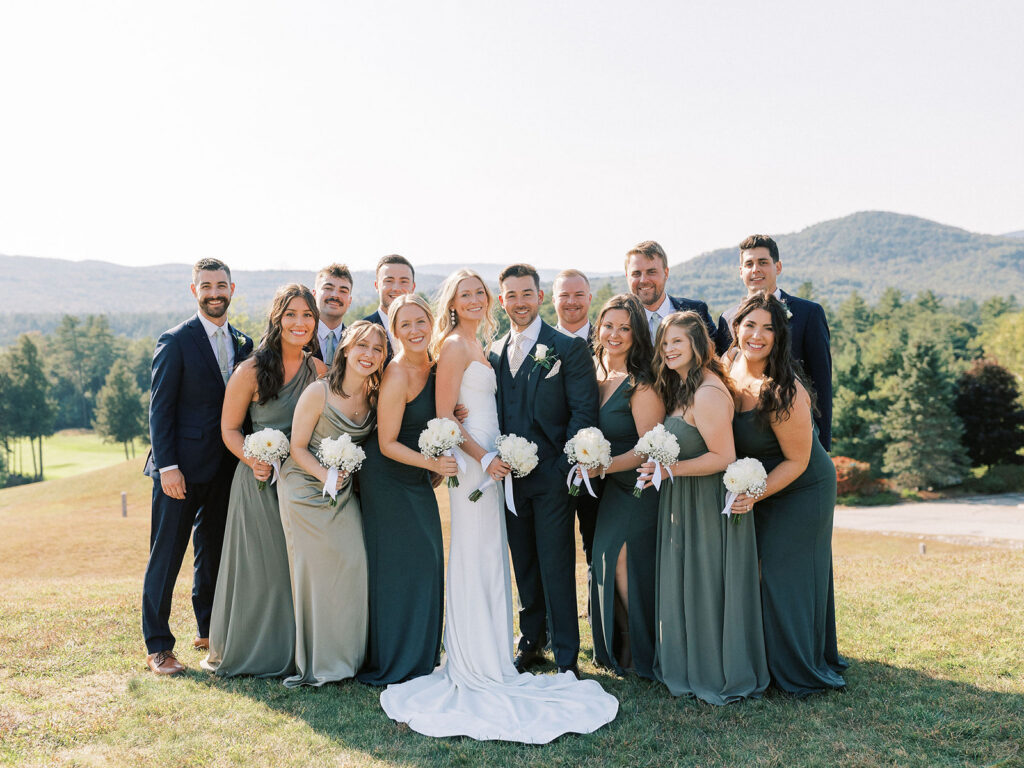 Bride and groom standing with their wedding party outdoors with mountain landscape in the background.