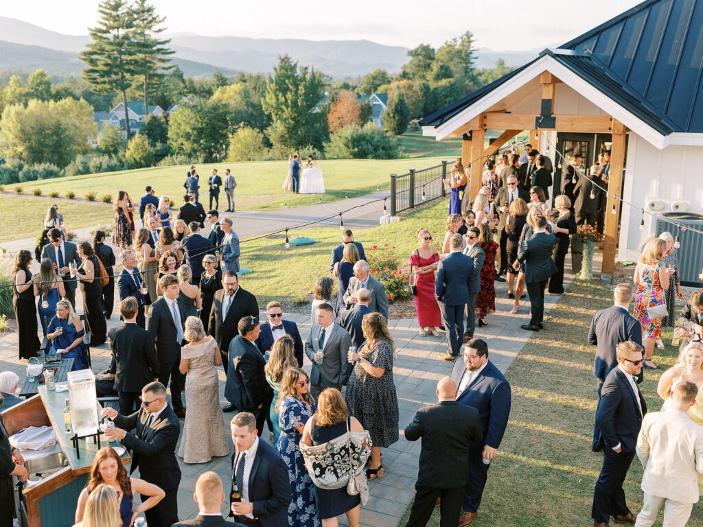 Wedding guests mingling and enjoying drinks during outdoor cocktail hour with mountain views in the background.