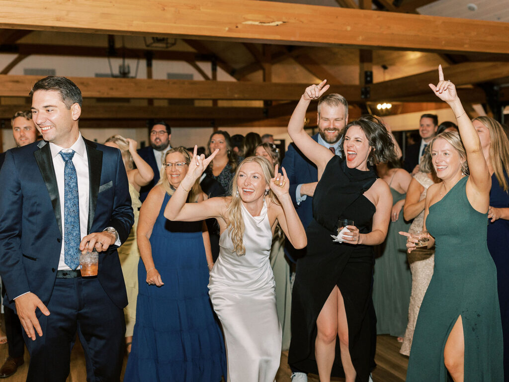 The bride dancing with hands raised alongside jubilant guests on a packed reception dance floor.
