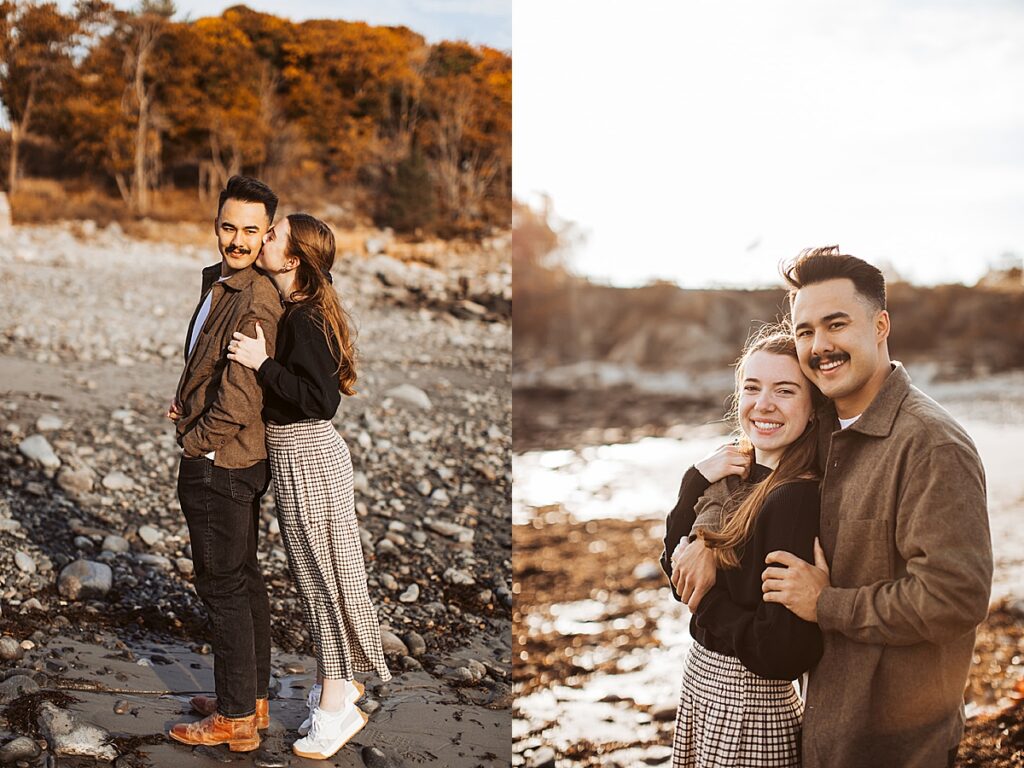 Engaged couple embracing on rocky Maine beach and smiling together near shoreline during golden hour engagement photos.