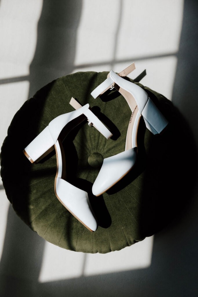 White bridal heels on green velvet chair with window light and shadows, elegant wedding detail at Wentworth Inn