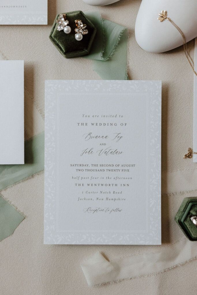Flat lay of wedding invitation, pearl earrings, and jewelry on soft fabric with green accents, Wentworth Inn details