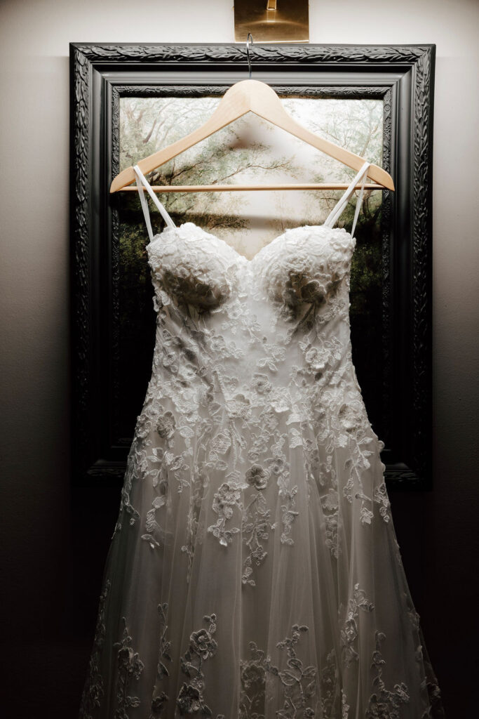 Lace wedding dress hanging on wooden hanger in front of framed artwork, bridal prep at Wentworth Inn