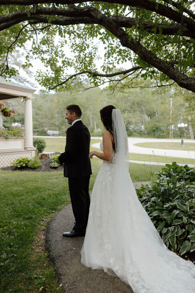 Bride approaching groom from behind for first look on garden path at Wentworth Inn