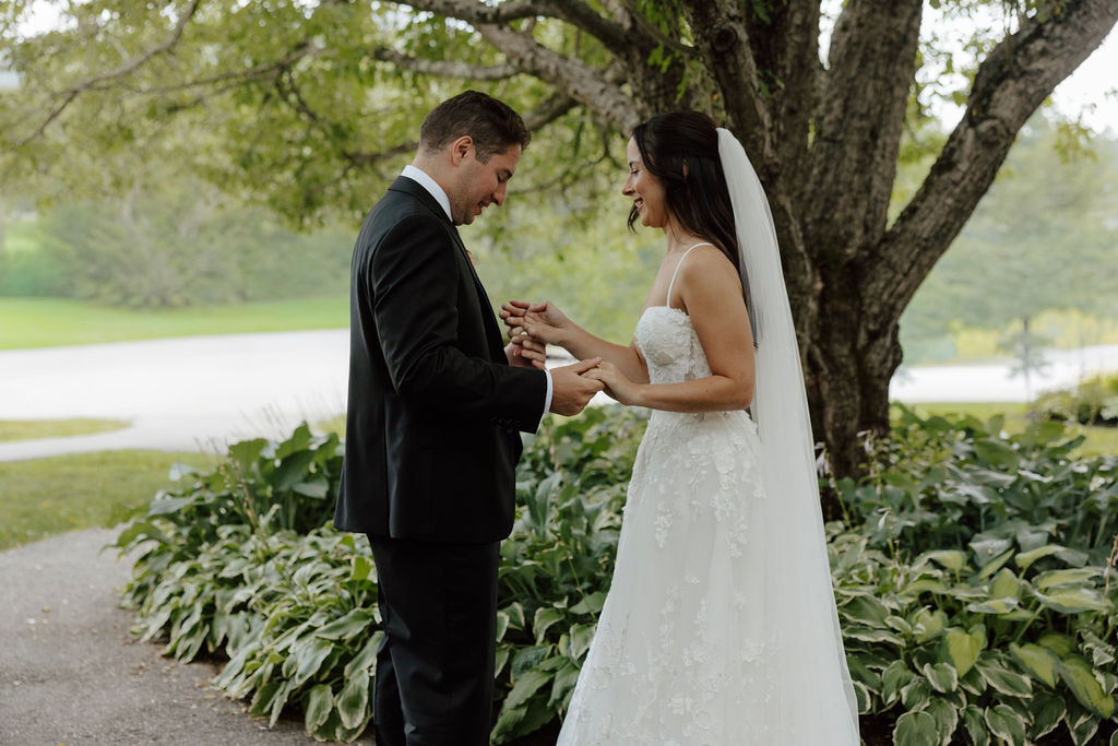 Bride and groom holding hands and smiling during first look under tree at Wentworth Inn