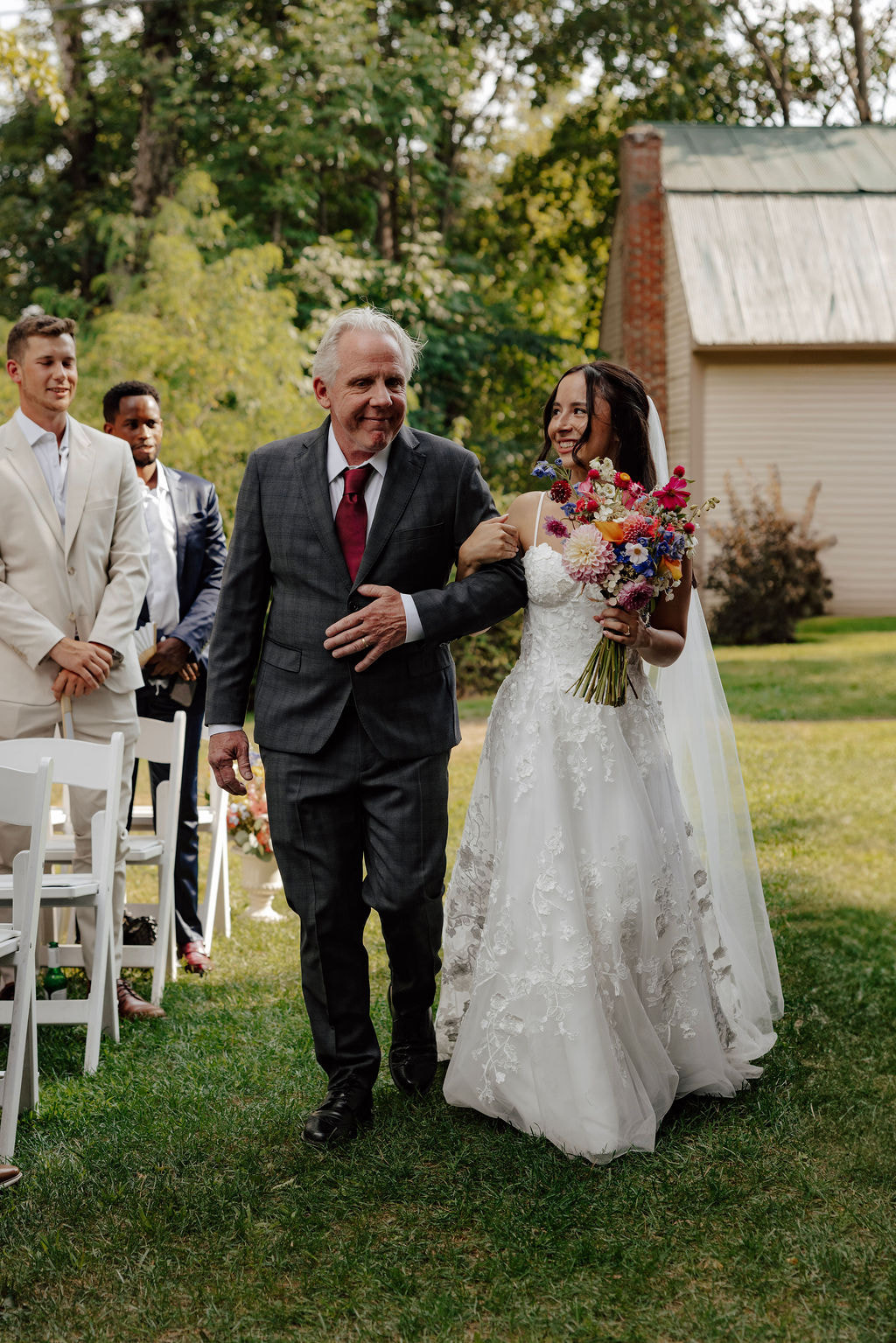 Bride walking down outdoor aisle with older man, holding colorful bouquet at Wentworth Inn wedding ceremony