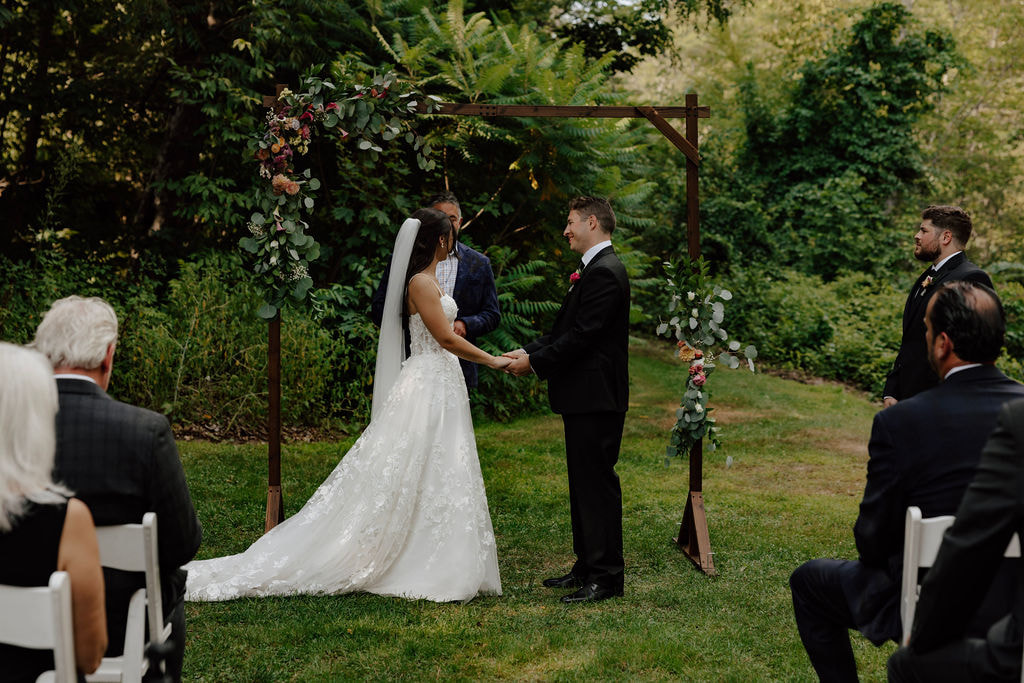 Bride and groom holding hands during outdoor ceremony under floral arch at Wentworth Inn