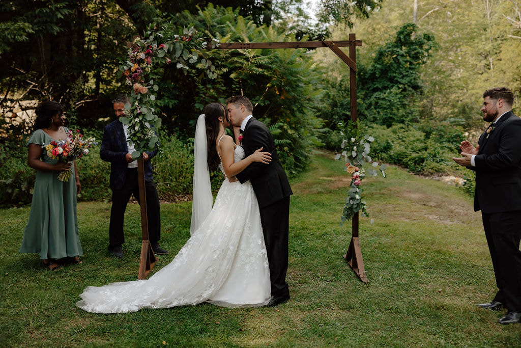 Bride and groom sharing first kiss under floral arch during outdoor garden ceremony