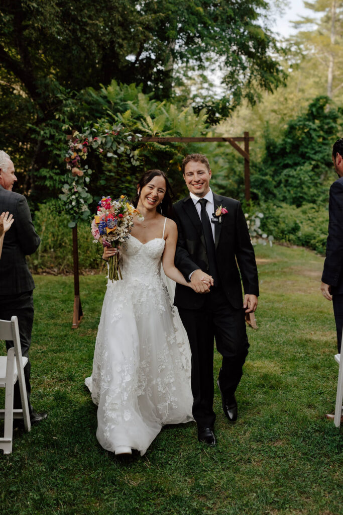 Newlyweds walking down aisle smiling after ceremony, guests applauding at Wentworth Inn