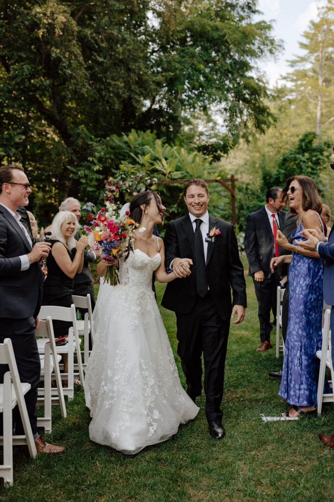 Bride and groom recessional down aisle with guests cheering on garden lawn