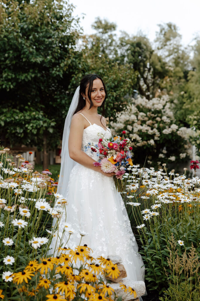 Bride standing in garden with colorful bouquet among blooming flowers at Wentworth Inn