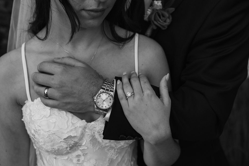 Close-up of couple’s hands showing wedding rings and watch, intimate black and white detail