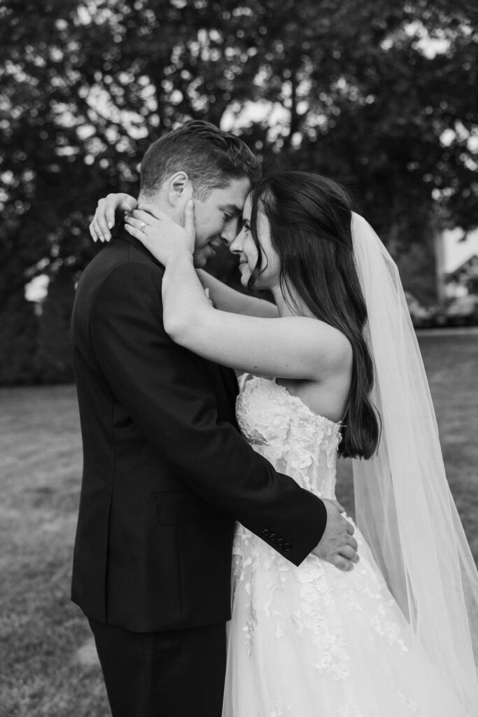 Black and white portrait of bride and groom embracing closely, intimate wedding moment outdoors